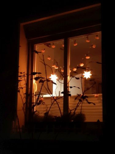 Blick von außen in ein Zimmerfenster mit weihnachtlicher Beleuchtung